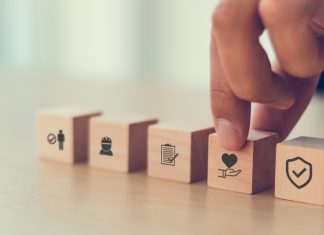 Why is Occupational Health Important? Safety at work concept. Hand holds cubes wooden block with safety icons; safety first, protections, health, regulations and insurance. Used for banner, beautiful bright background and copy space.