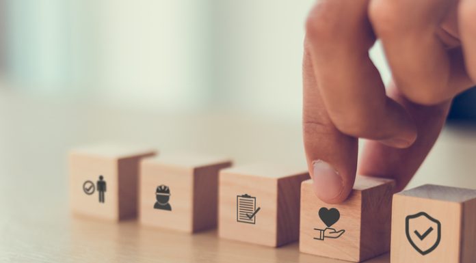 Safety at work concept. Hand holds cubes wooden block with safety icons; safety first, protections, health, regulations and insurance. Used for banner, beautiful bright background and copy space.