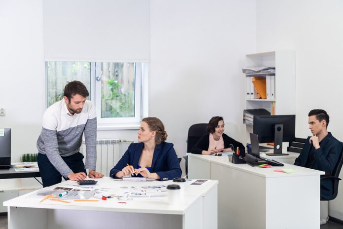 Office workers in an open space, doing different things, colleagues chatting, discussing projects, working on PCs, doing some paperwork. Coworking concept LLC