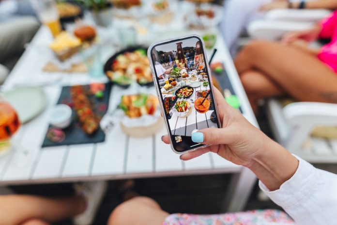 Close-up shot of a girl holding a phone and photographing the table with delicious food Restaurant Sector