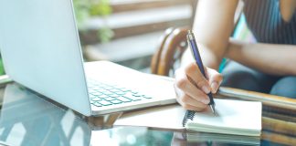 WriteMyPapers Review: Best Professional Academic Writing Help Business woman hand is writing on a notepad with a pen and using a laptop computer.