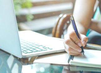 WriteMyPapers Review: Best Professional Academic Writing Help Business woman hand is writing on a notepad with a pen and using a laptop computer.