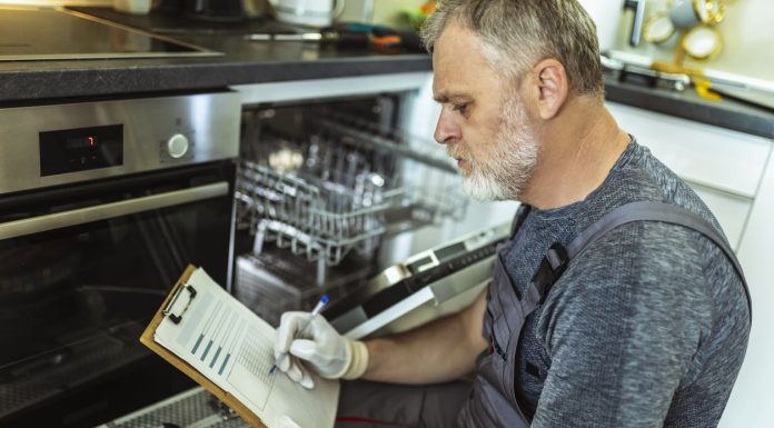 Hazard Analysis and Critical Control Point (HACCP) Explained Male Technician Sitting Near Dishwasher Writing On Clipboard In Kitchen