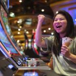 exited asia female woman slot machine gambling cheerful smile hand pressing bet button in casino club entertainment concept,exited asian woman hand play slot machine in casino hotel
