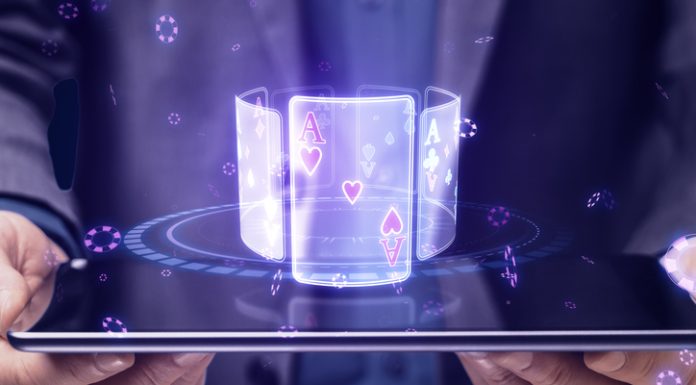Close up of businessman hands holding tablet with creative digital blue cards hologram on dark background. Online casino, poker and digital gaming concept.