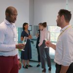 Side view of cheerful multicultural businessmen holding champagne glasses and talking in the event