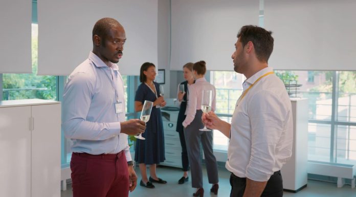 Side view of cheerful multicultural businessmen holding champagne glasses and talking in the event