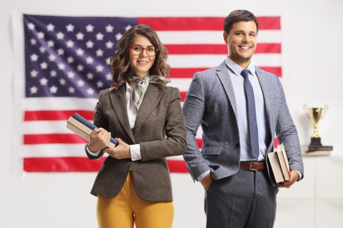 Young man and woman holding books in front of USA flag