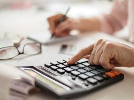 Pension calculation concept, old hands counting finances on a home calculator , close- up