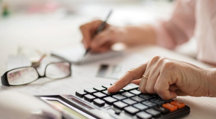 Pension calculation concept, old hands counting finances on a home calculator , close- up