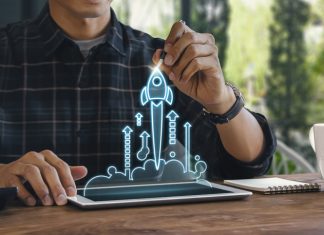 Business start up, start, new project or new idea concept. Wooden blocks with launching rocket graphic arranged in pyramid shape and a man is holding the top one.