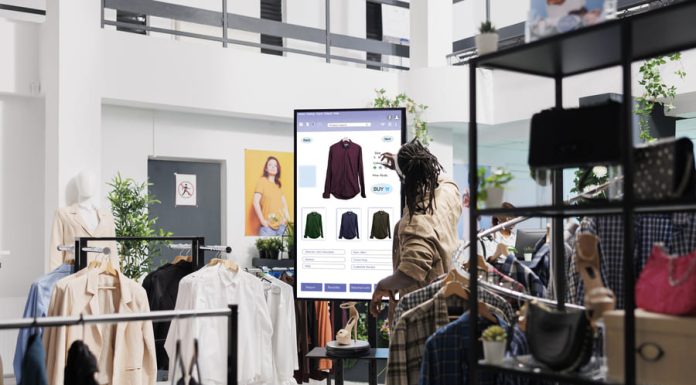 African american man looks at clothes online on touch screen monitor in fashion boutique at mall