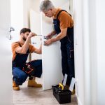Locksmiths in London: A Guide to Trusted Services and Security Solutions Best men at work. Full length shot of two locksmith, repairmen, workers in uniform installing, working with house door lock using screwdriver.