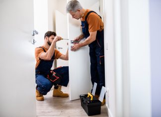 Best men at work. Full length shot of two locksmith, repairmen, workers in uniform installing, working with house door lock using screwdriver.