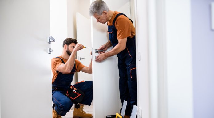 Best men at work. Full length shot of two locksmith, repairmen, workers in uniform installing, working with house door lock using screwdriver.