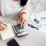 woman writing a list of debt on notebook calculating her expenses with calculator