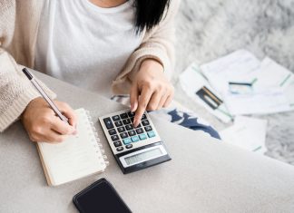 woman writing a list of debt on notebook calculating her expenses with calculator