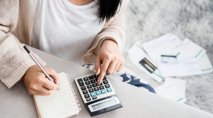 woman writing a list of debt on notebook calculating her expenses with calculator