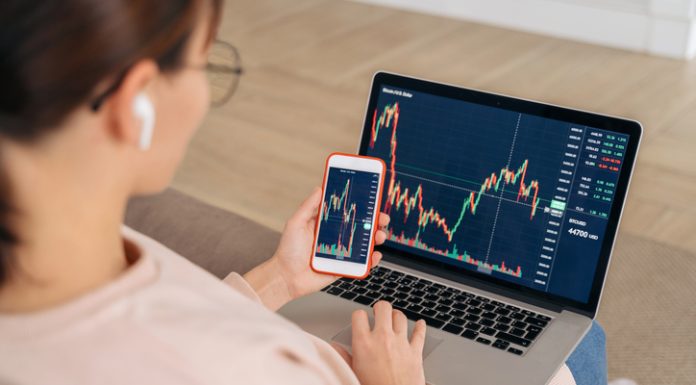 woman looking at financial stock market using cellphone and laptop