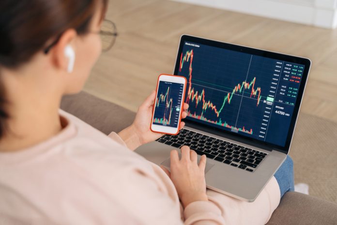 woman looking at financial stock market using cellphone and laptop