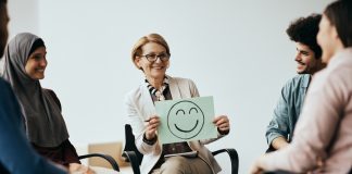 Workplace and Mental Health: Building Effective Leaders by Enhancing Cognitive Behaviour Therapy Breaks the Toxic Work Culture Professional holding a placard with drawn smiley face while discussing Workplace Mental Health.