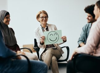 Workplace and Mental Health: Building Effective Leaders by Enhancing Cognitive Behaviour Therapy Breaks the Toxic Work Culture Professional holding a placard with drawn smiley face while discussing Workplace Mental Health.