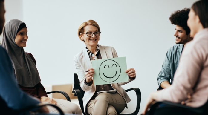 Workplace and Mental Health: Building Effective Leaders by Enhancing Cognitive Behaviour Therapy Breaks the Toxic Work Culture Professional holding a placard with drawn smiley face while discussing Workplace Mental Health.