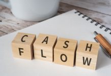 Wooden blocks with "CASH FLOW" text of concept, a pen, a notebook, and a cup.