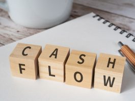 Wooden blocks with "CASH FLOW" text of concept, a pen, a notebook, and a cup.