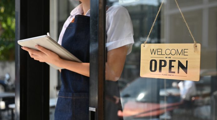 How to Open a Cafe in 2024: The Ultimate Guide woman standing at coffee shop entrance