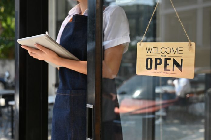 cropped image, Female barista or coffee shop owner stands at her coffee shop's entrance door woman standing at coffee shop entrance