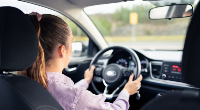Woman driving car. Young driver. Testing vehicle in dealership or student training in school to get license. Hands on steering wheel. Behind back inside view of cockpit.