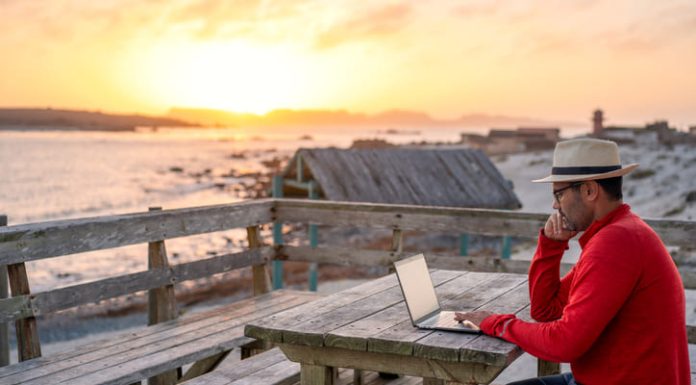 A man working on a laptop outdoors at the beach. A man working on a laptop outdoors at the beach.