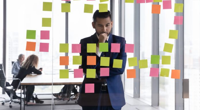 Young pensive Indian businessman in suit stand near glass wal