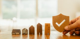 Wooden house model and real estate insurance ideas, and small shield icon.