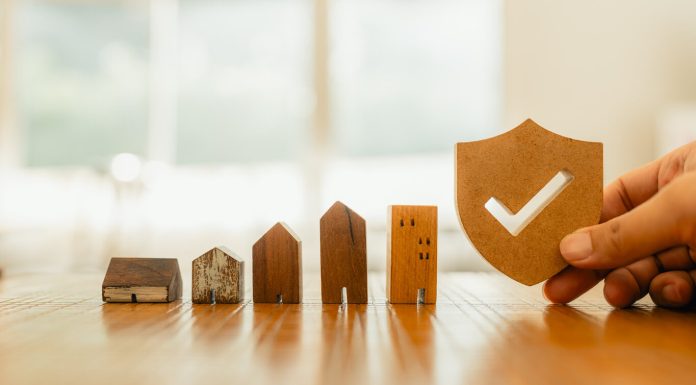 Term vs Permanent Life Insurance: Making the Choice For 2024 Wooden house model and real estate insurance ideas, and small shield icon.