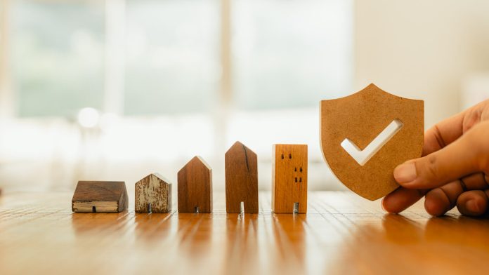 Wooden house model and real estate insurance ideas, and small shield icon.