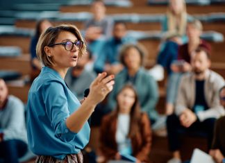 Corporate Leadership Training Mid adult businesswoman talking to group of seminar attendees in conference hall.