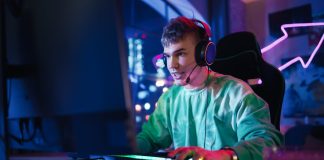 Gaming at Home: Portrait of a Gamer Wearing Headphones and Playing Online Game on Personal Compute