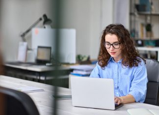 Woman employee sitting at desk working online on laptop