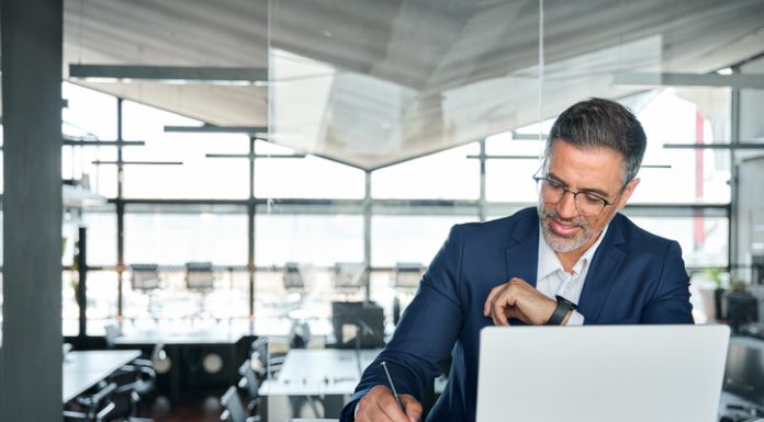 Mid aged business man working on laptop computer in office writing notes.