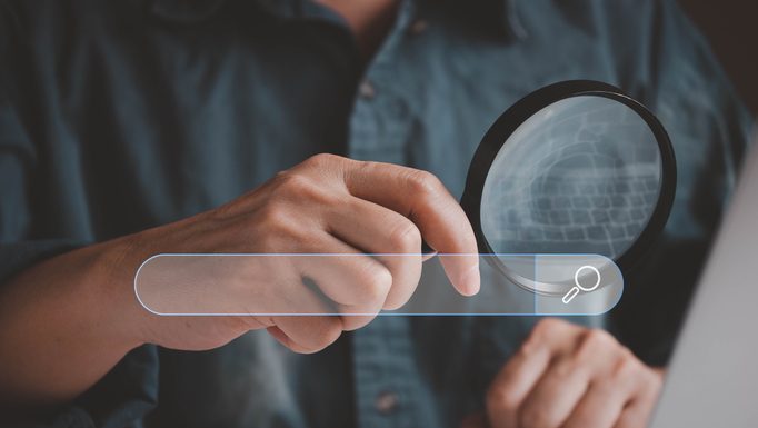 Man holding magnifying glass while using computer