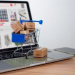 Shopping cart and product boxes placed on laptop computer for e-commerce