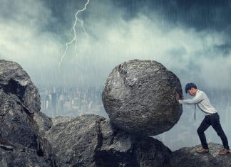 Business man pushing large stone up to hill