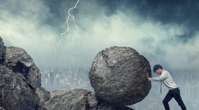 Business man pushing large stone up to hill