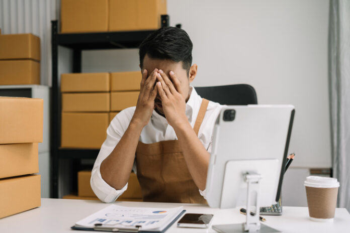 Young sad Entrepreneur is sitting at table, covering his face. small online business owner, Stress. Small online business owner, Stress.