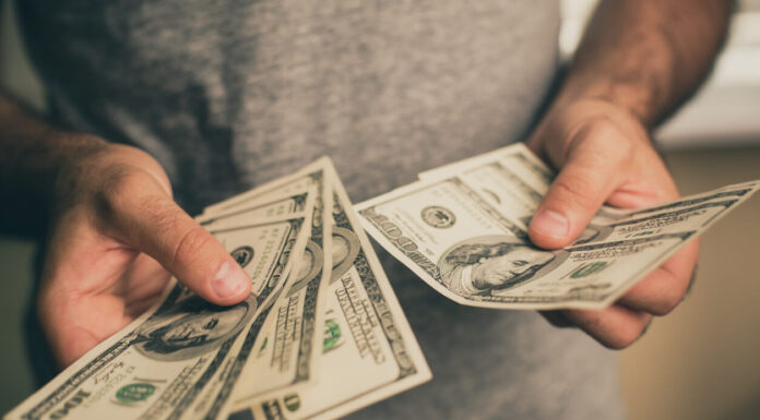 A man in a gray T-shirt holds dollars in his hands. Bank. Casino. Salary. Rates