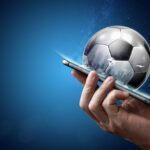Why Football Betting is Increasing Day by Day? Smartphone in hand with a 3D soccer ball on a blue background