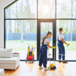 The Impact of Professional Cleaning Services on Home Health Young cleaners in blue uniform mopping wooden floor and cleaning big panoramic window