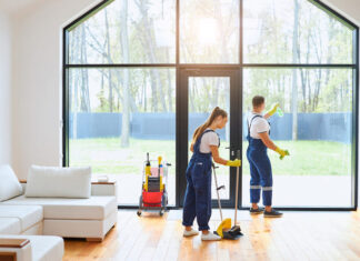 Young cleaners in blue uniform mopping wooden floor and cleaning big panoramic window